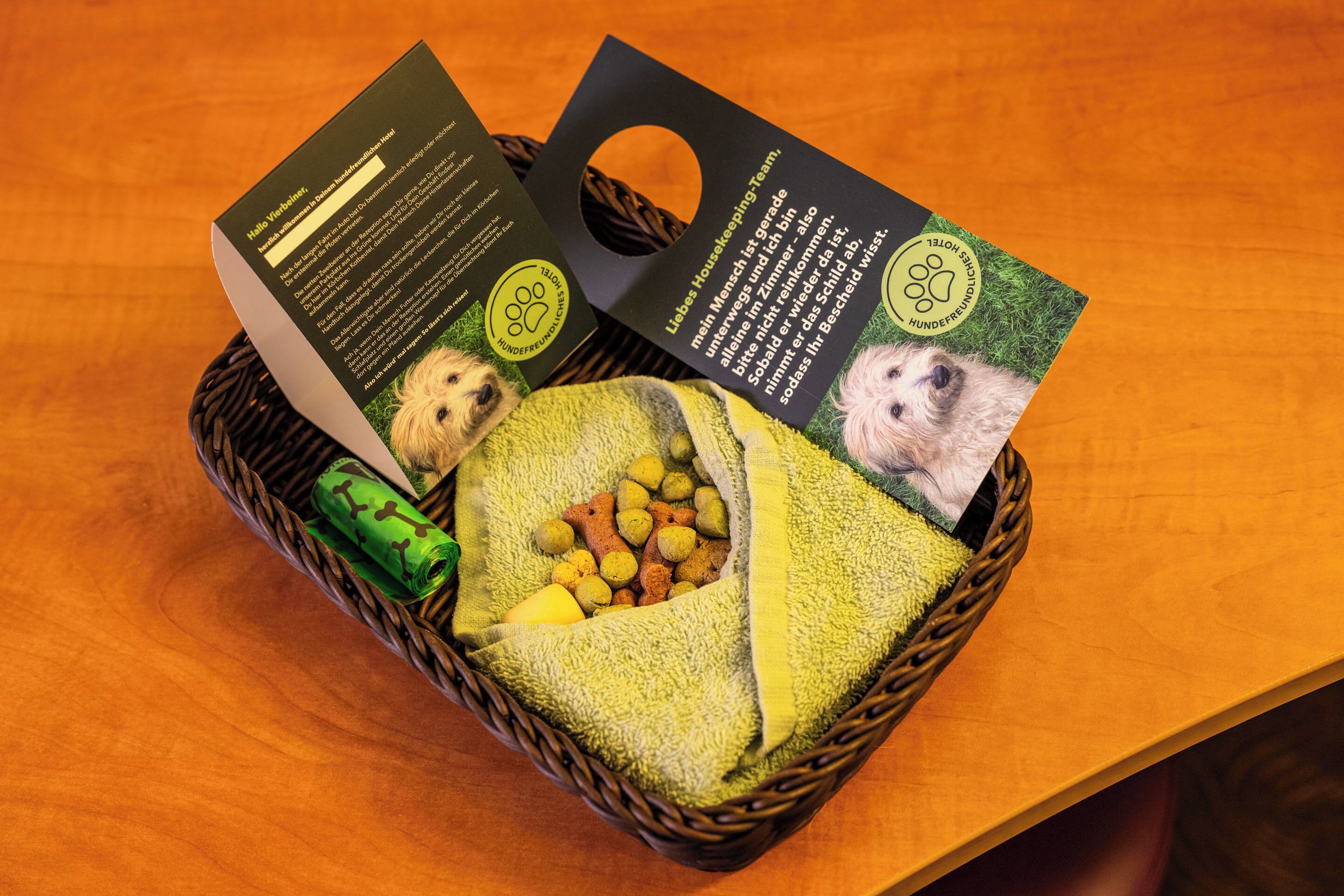 A wicker basket containing a green towel, a green roll, and a bag of dog treats.