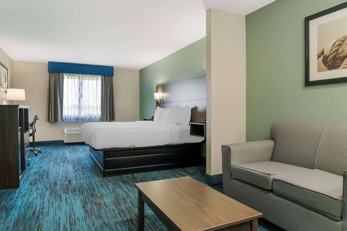 A hotel room with a bed, a sofa, a wooden table, and a desk with a lamp.