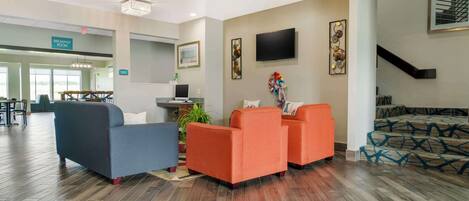 A hotel lobby with a breakfast area, seating with a TV, and a staircase.