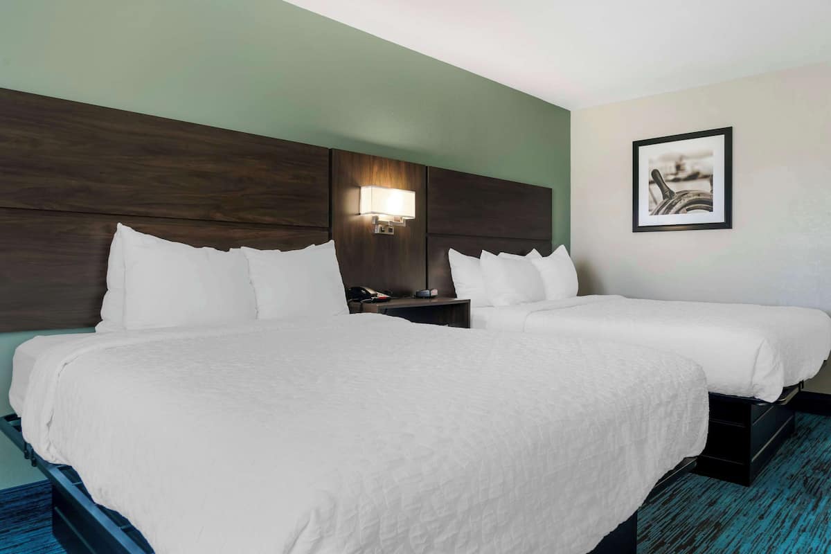 A hotel room with two beds, a nightstand, a lamp, and a framed picture on the wall.
