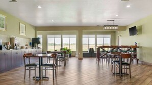 A spacious dining area with multiple tables and chairs, large windows offering a view of the outdoors, and a kitchen area with modern appliances. - Best Western Clare Hotel (Clare)