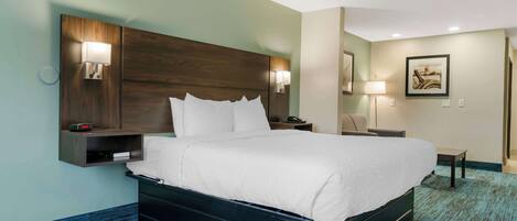 A hotel room with a large bed, bedside lamps, a nightstand, a wall-mounted shelf, and a framed picture on the wall.