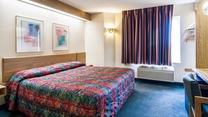 Una camera d'hotel con un letto, una scrivania, una sedia, una finestra con tende e due opere d'arte appese al muro.