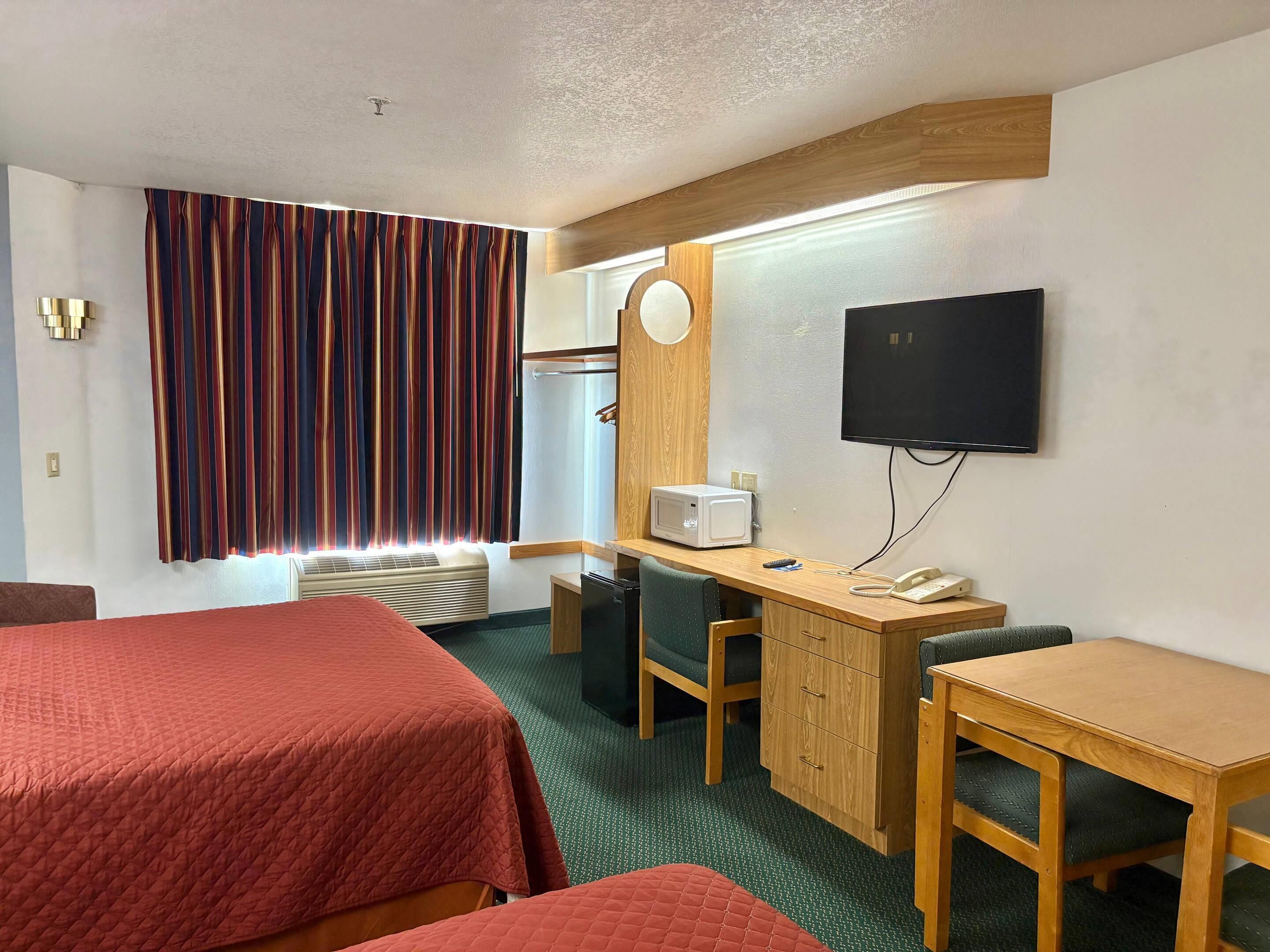 A hotel room with two beds, a desk, a chair, a microwave, a TV, and a small refrigerator.