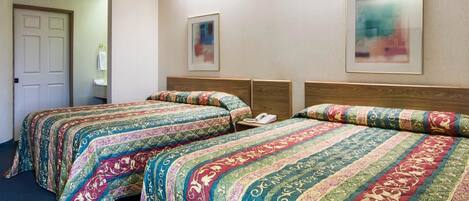 Habitación de hotel con dos camas, cada una con una colcha estampada, una mesita de noche con un teléfono y un cuadro abstracto enmarcado en la pared.