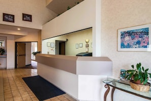 A hotel reception area with a reception desk, framed pictures on the walls, a large mirror, and a potted plant on a glass table.
