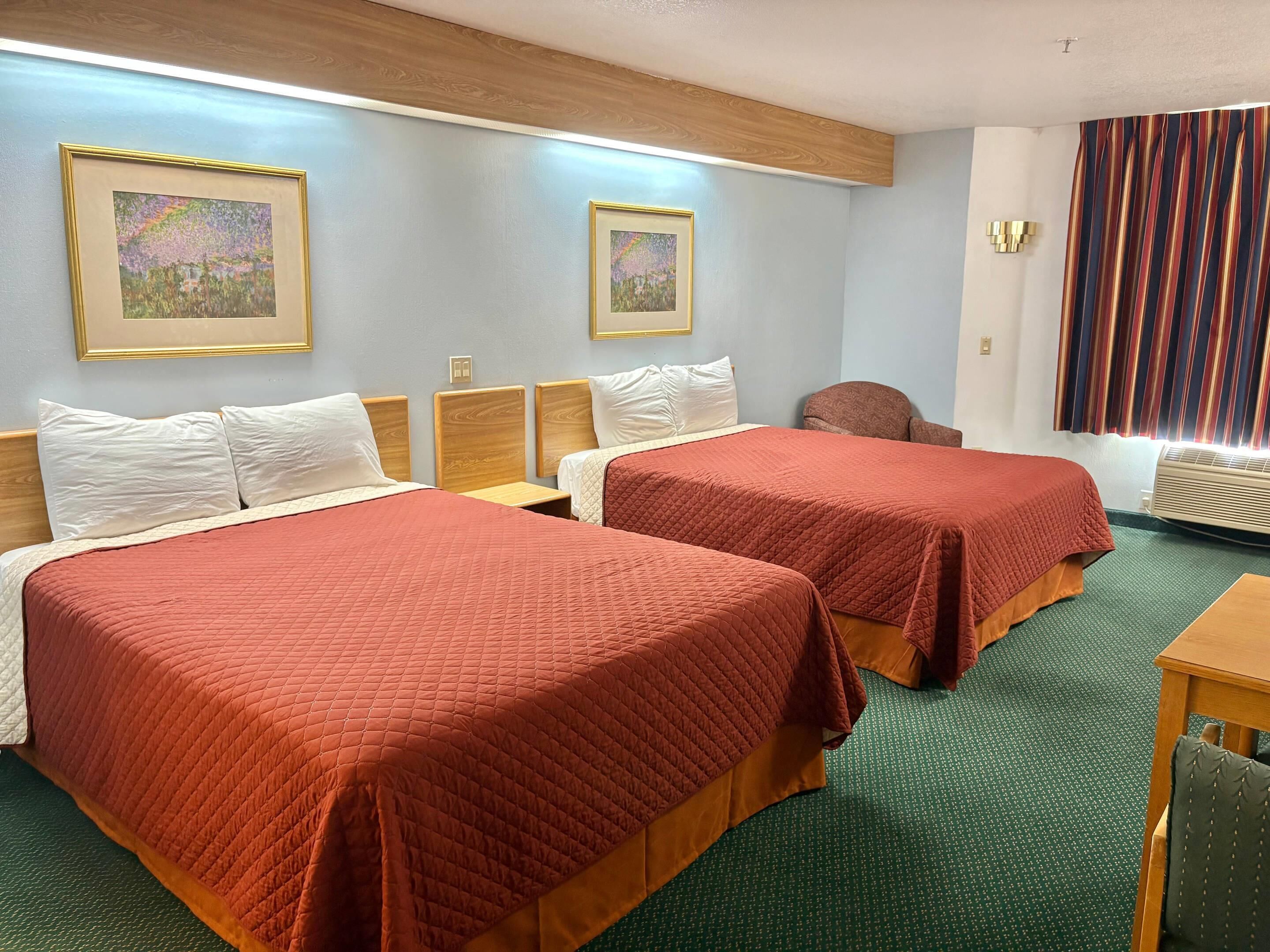 Een hotelkamer met twee bedden, een bureau, een stoel en twee ingelijste kunstwerken aan de muur.