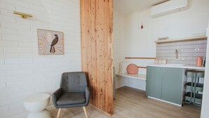A modern kitchen with white brick walls, a wooden accent wall, a grey chair, and a kitchen island with storage. - The Ellson Hotel (Kingscote)