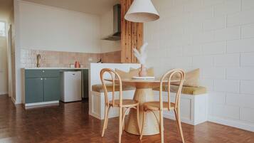 A compact kitchen with wooden cabinets, a dining area with a round table and chairs, and a white brick wall.