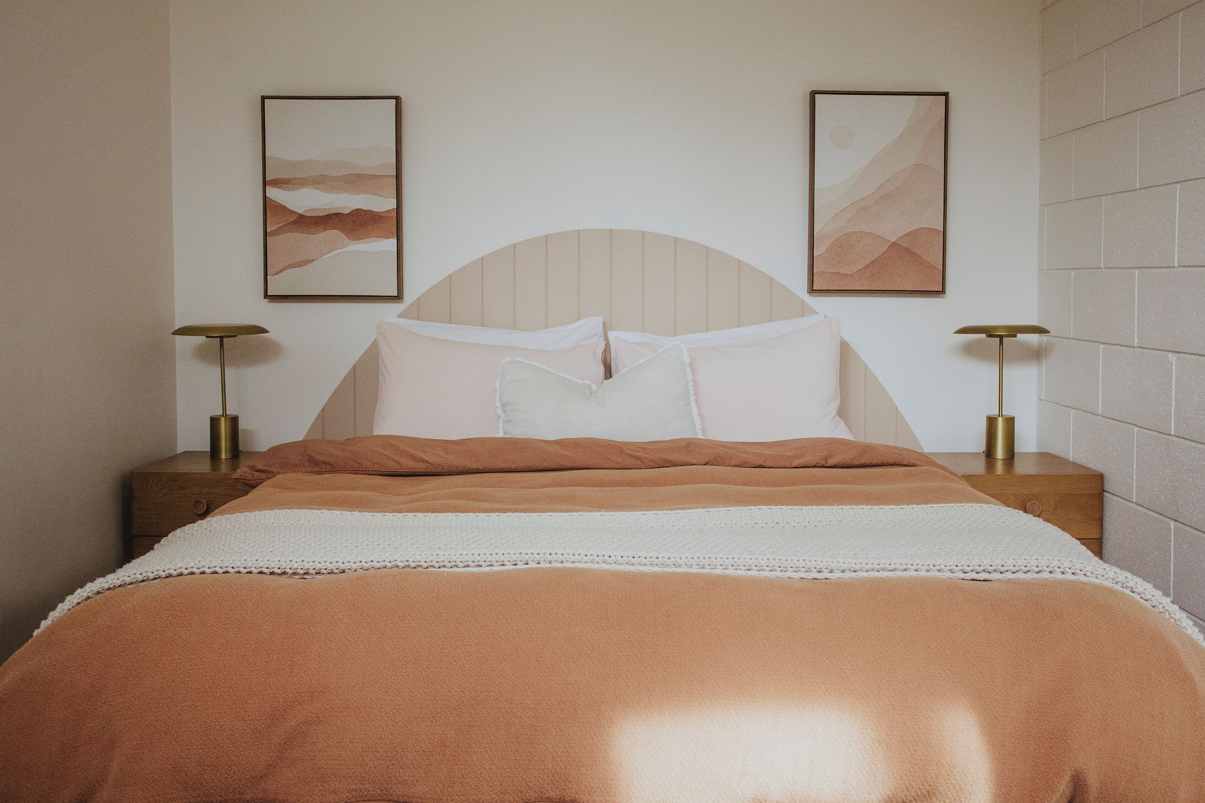 A neatly made bed with a headboard, two bedside tables with lamps, and two framed artworks on the wall.