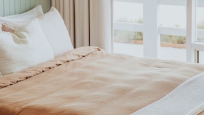 A bed with a beige blanket, a white pillow, and a shelf above it. - The Ellson Hotel (Kingscote)
