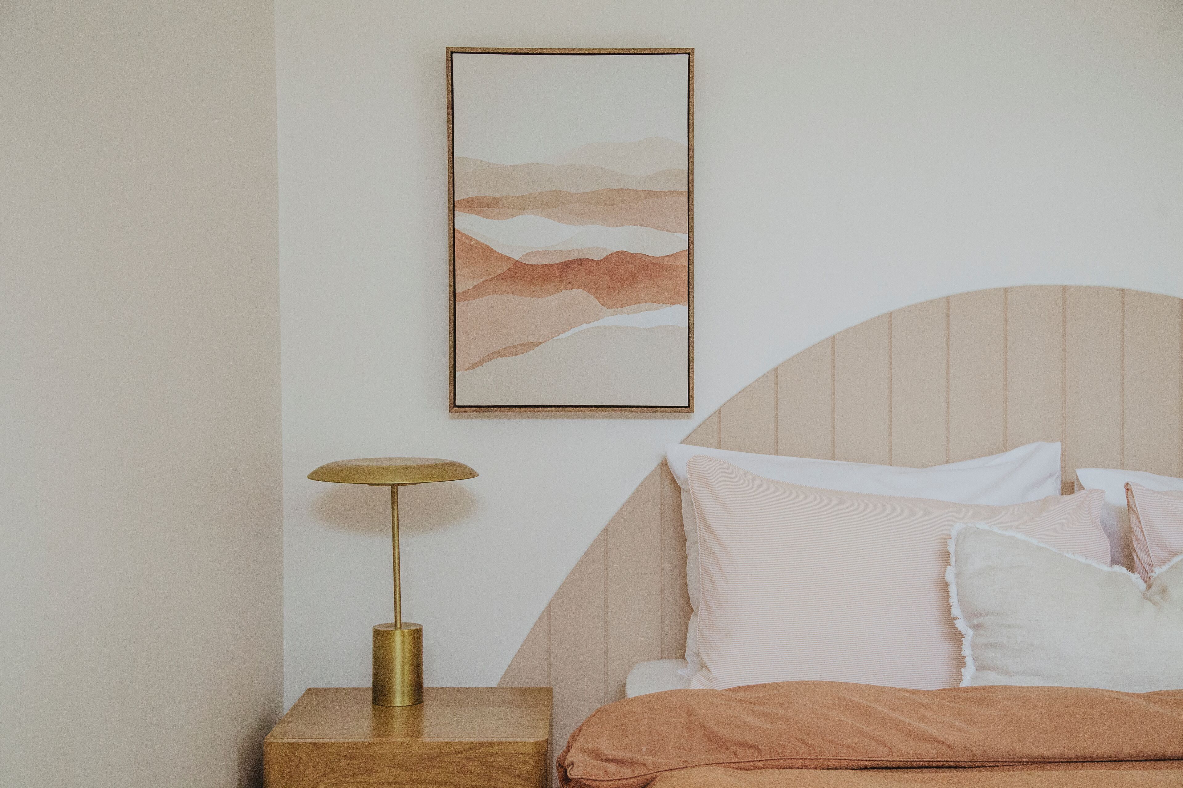 A bedroom with a bed, a bedside table with a lamp, and a wall-mounted artwork.