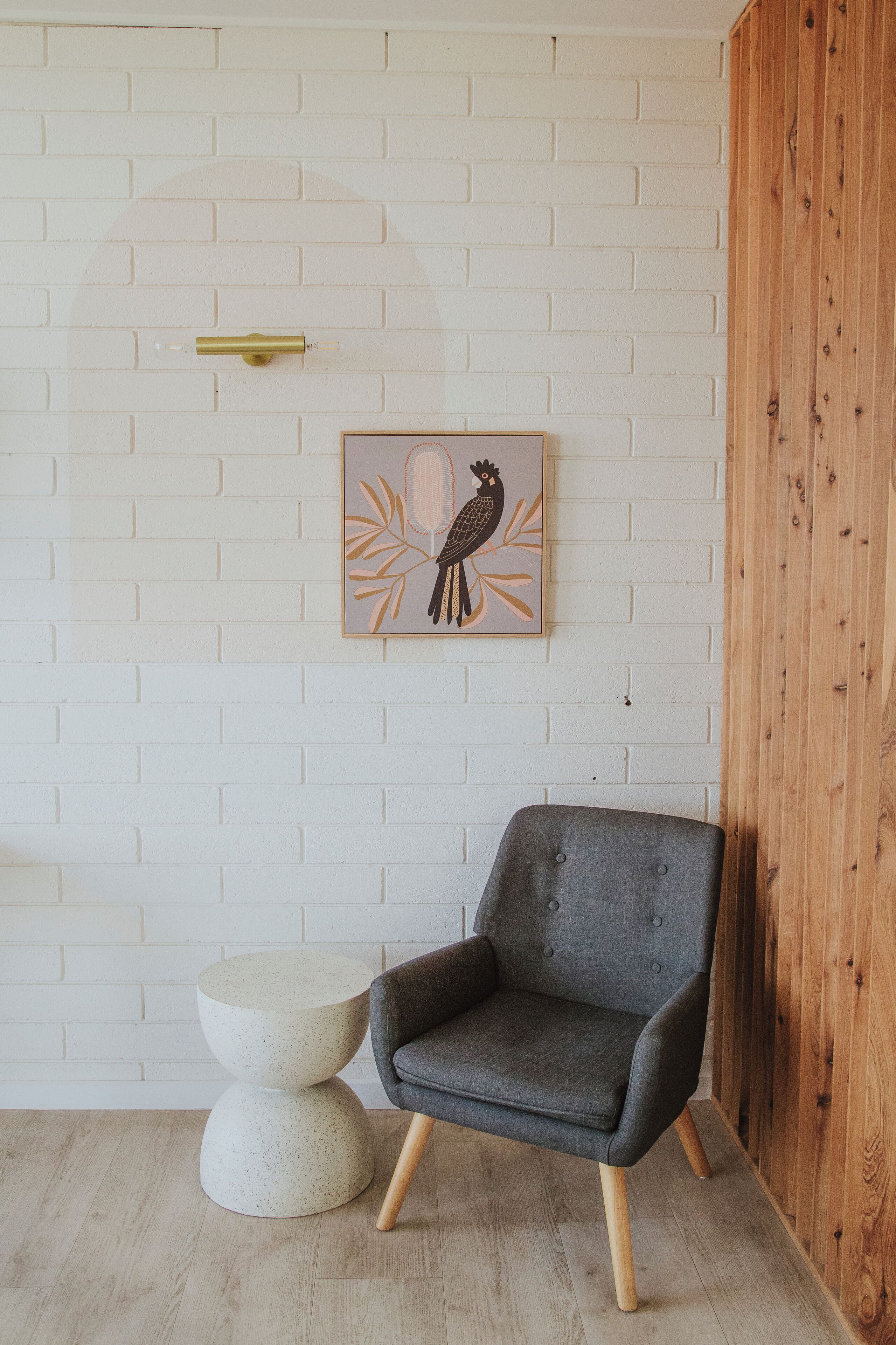 A modern room with a grey upholstered armchair, a round white side table, and a wooden cabinet.