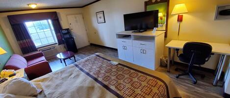A hotel room with a bed, a desk, a chair, a television, a small table, and a window with curtains.