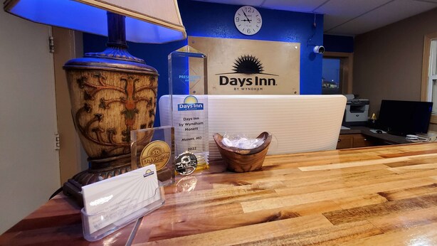 Een receptiebalie met een klok, een plaquette en een lijst met het bord Days Inn.