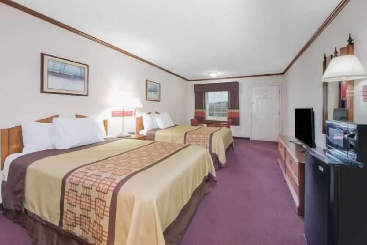 A hotel room with two beds, a television, a desk, and a window.