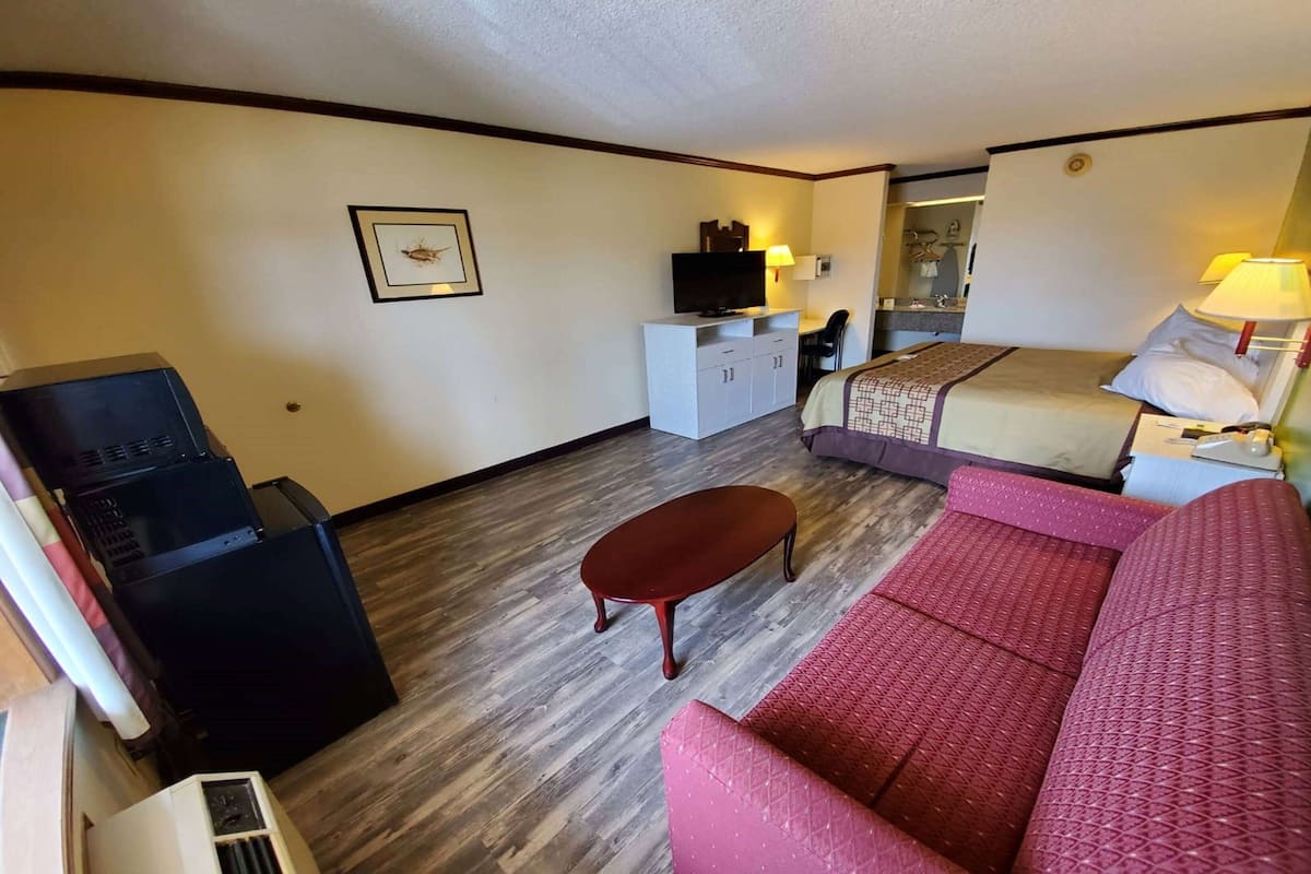 A hotel room with a bed, a red sofa, a small table, a TV on a cabinet, and a mirror.