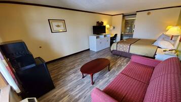 A hotel room with a bed, a red sofa, a small table, a TV on a cabinet, and a mirror.