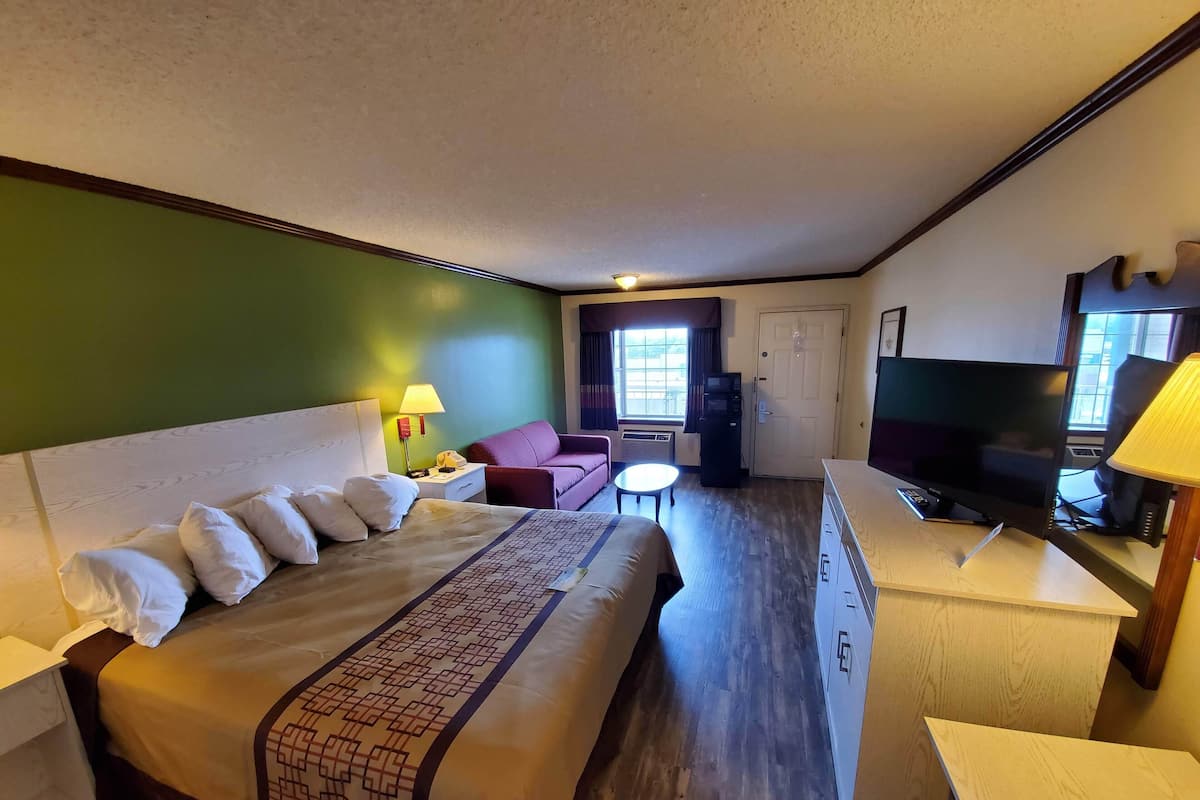 A hotel room with a large bed, a desk with a TV, a sofa, and a small table.