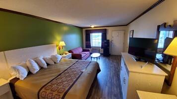 A hotel room with a large bed, a desk with a TV, a sofa, and a small table.
