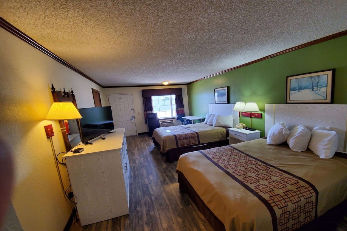 A hotel room with two beds, a desk, a television, and a window with curtains.