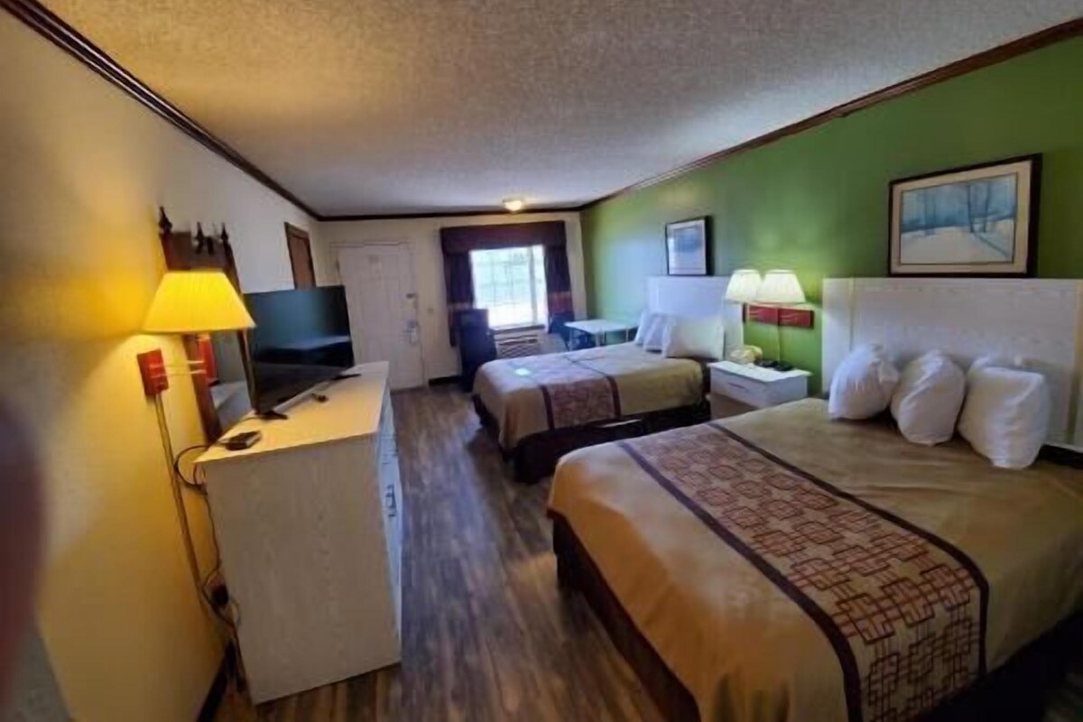 Una camera d'albergo con due letti, una scrivania, una televisione e una finestra.