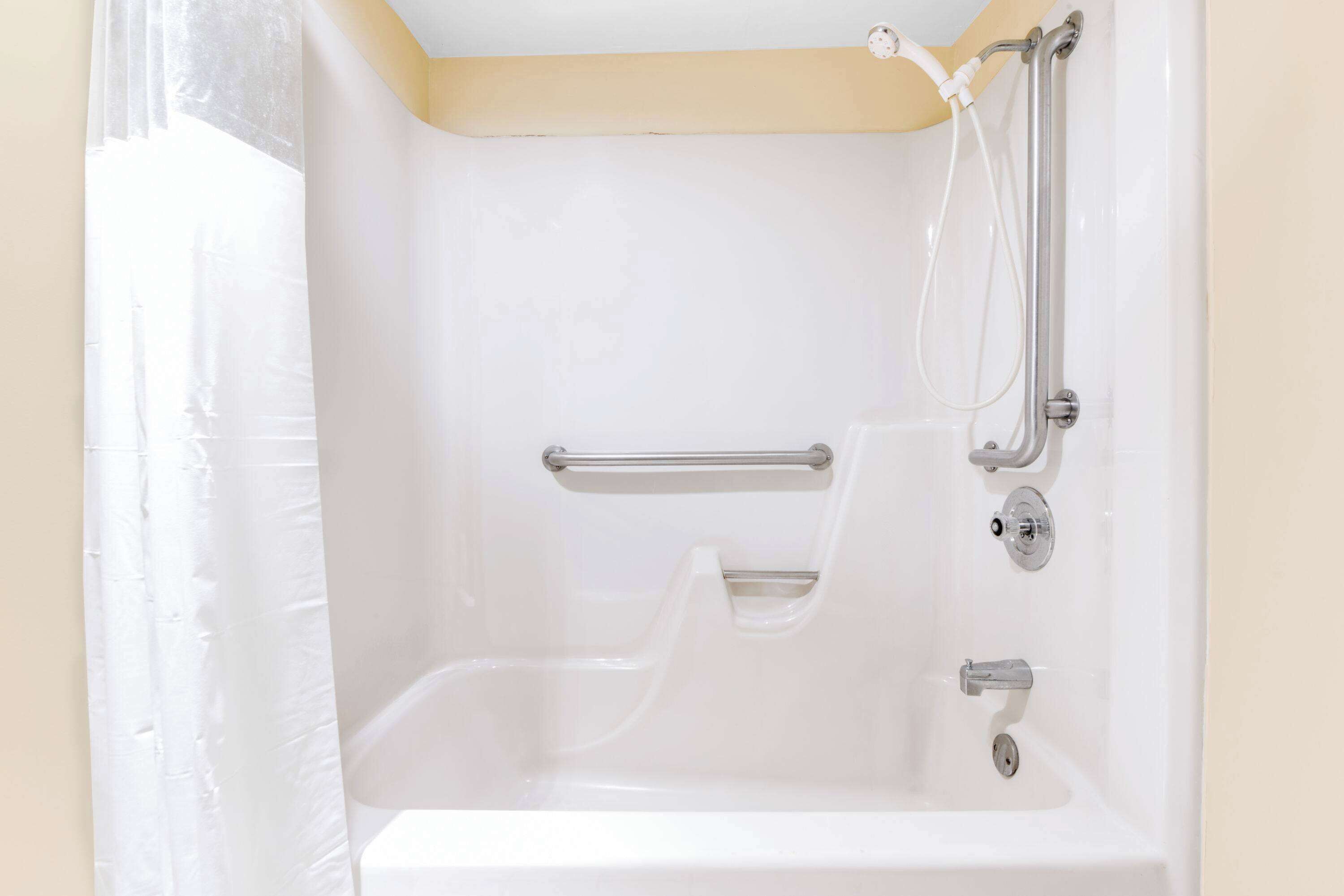 A white bathtub with a handheld showerhead and grab bars.