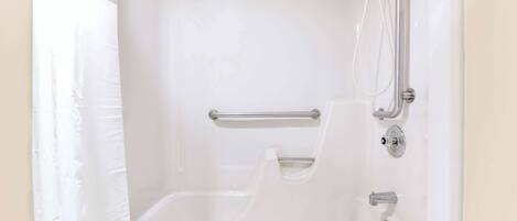 A white bathtub with a handheld showerhead and grab bars.