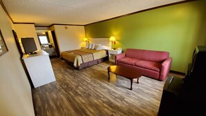 Een hotelkamer met een bed, een rode bank, een tafeltje, een bureau met een lamp en een televisie.