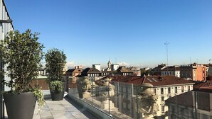 A rooftop terrace with potted plants, a glass railing, and a view of surrounding buildings. - Hotel Cristoforo Colombo – Preferred Hotels & Resorts (Milan)