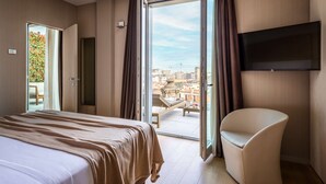 A hotel room with a bed, a chair, a TV, and a balcony with a view of the city. - Hotel Cristoforo Colombo – Preferred Hotels & Resorts (Milan)