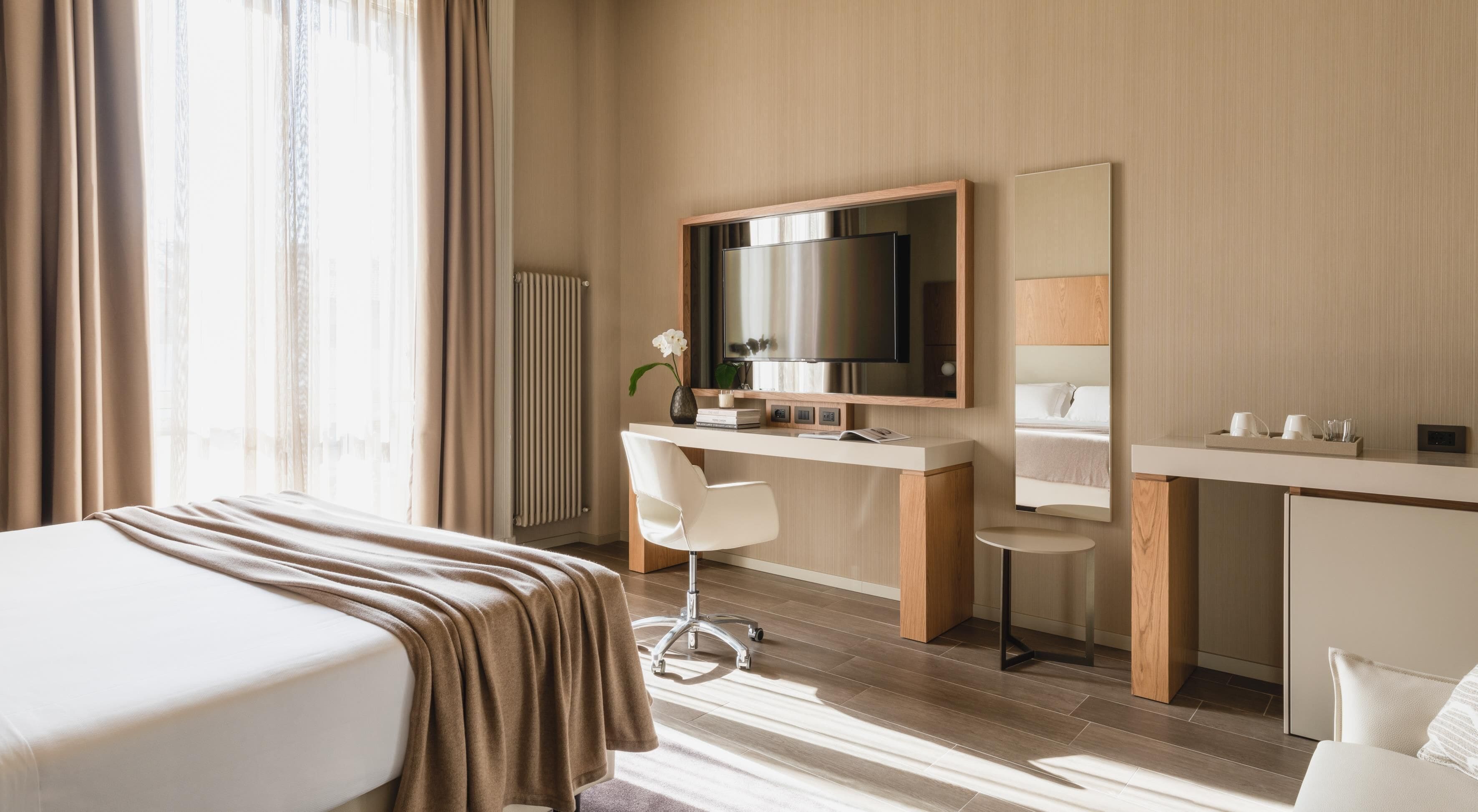 Een hotelkamer met een bed, een bureau, een stoel, een televisie en een spiegel.