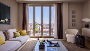 A modern living room with a sofa, a coffee table with a vase of flowers, a chair, and a view of the city through large sliding doors. - Hotel Cristoforo Colombo – Preferred Hotels & Resorts (Milan)