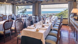 A dining area with tables set for a meal, overlooking a scenic view of the sea and hills. - Gran Hotel Rey Don Jaime (Castelldefels)