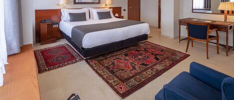 A hotel room with a bed, desk, chair, and two rugs.