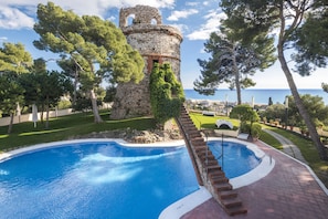 Una piscina con una torre de piedra, rodeada de árboles y vistas al mar.