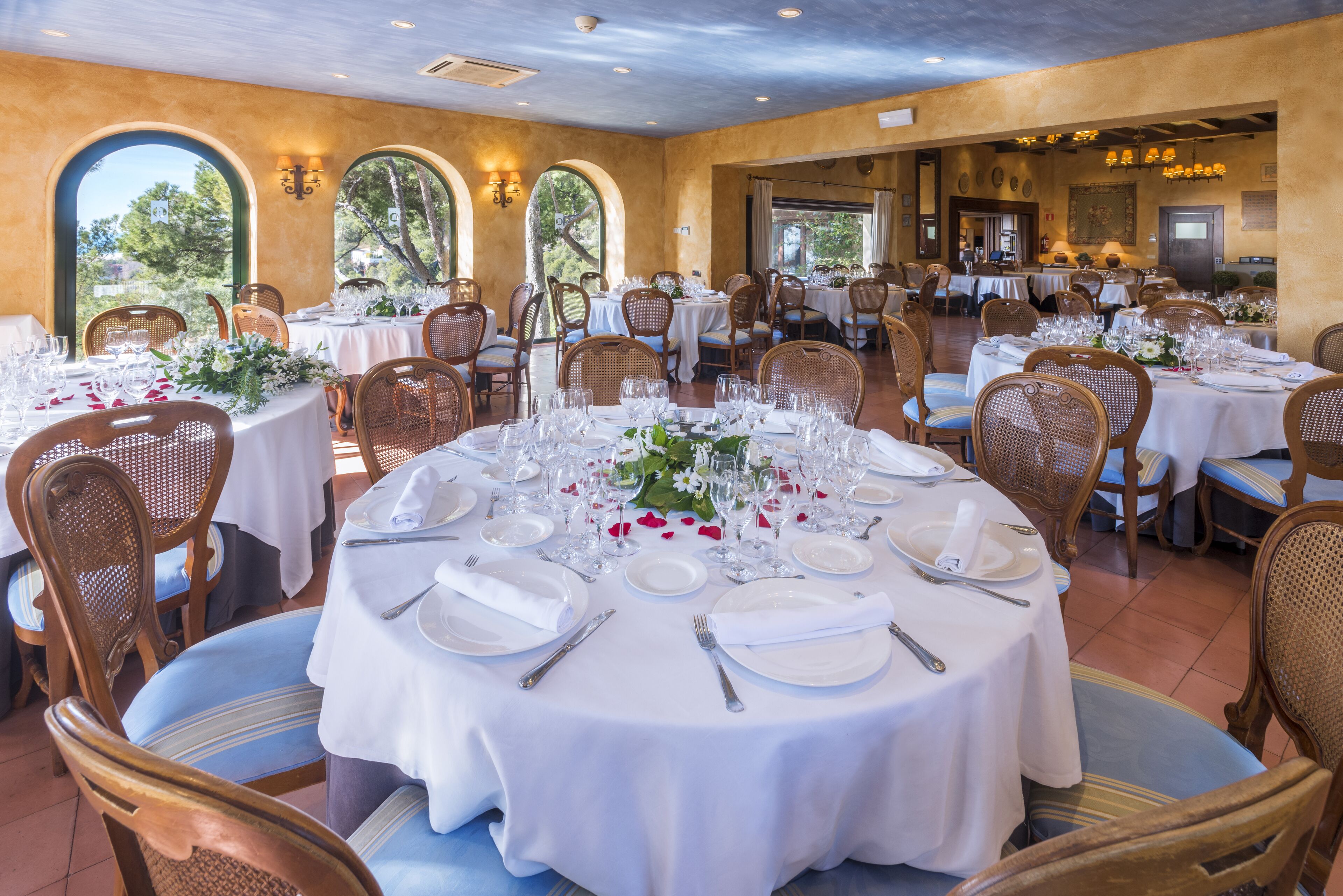 Un restaurante con mesas redondas dispuestas para comer, con manteles blancos y sillas de mimbre.