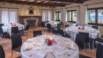 A dining area with round tables set for a meal, a fireplace, and a view of the sea.