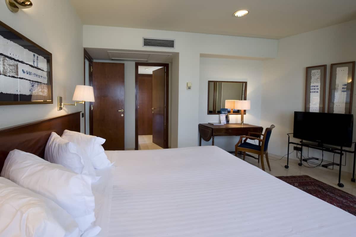 A hotel room with a large bed, a desk with a chair, a television, and a painting on the wall.