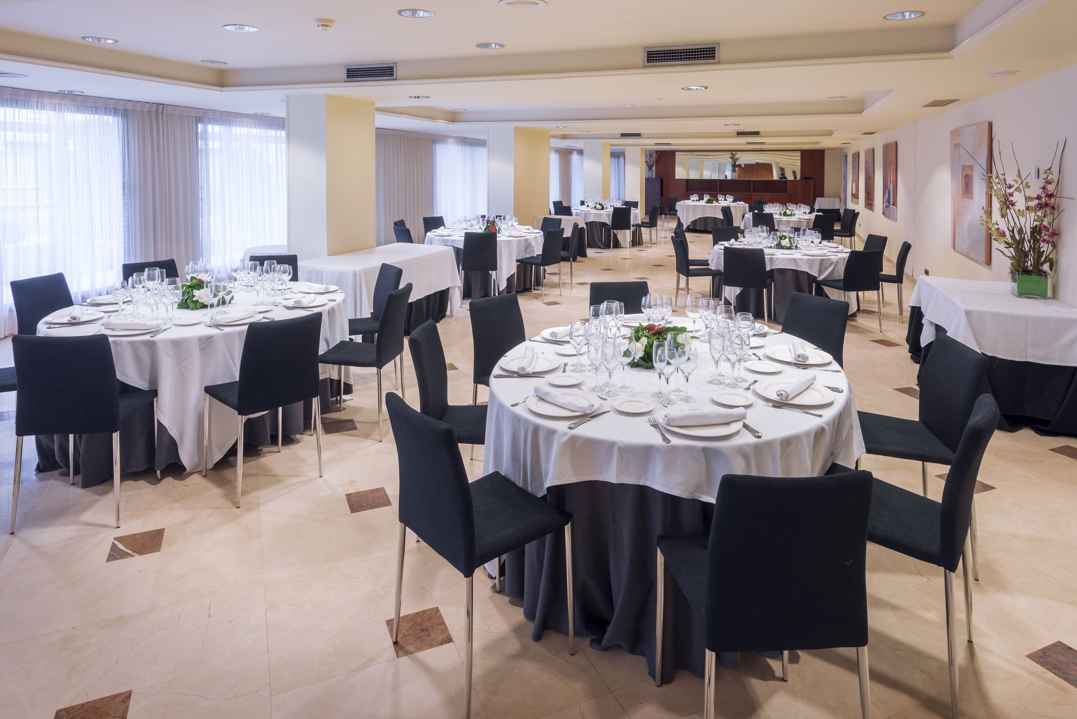 Un salón de banquetes con mesas redondas dispuestas para comer, sillas negras y manteles blancos.