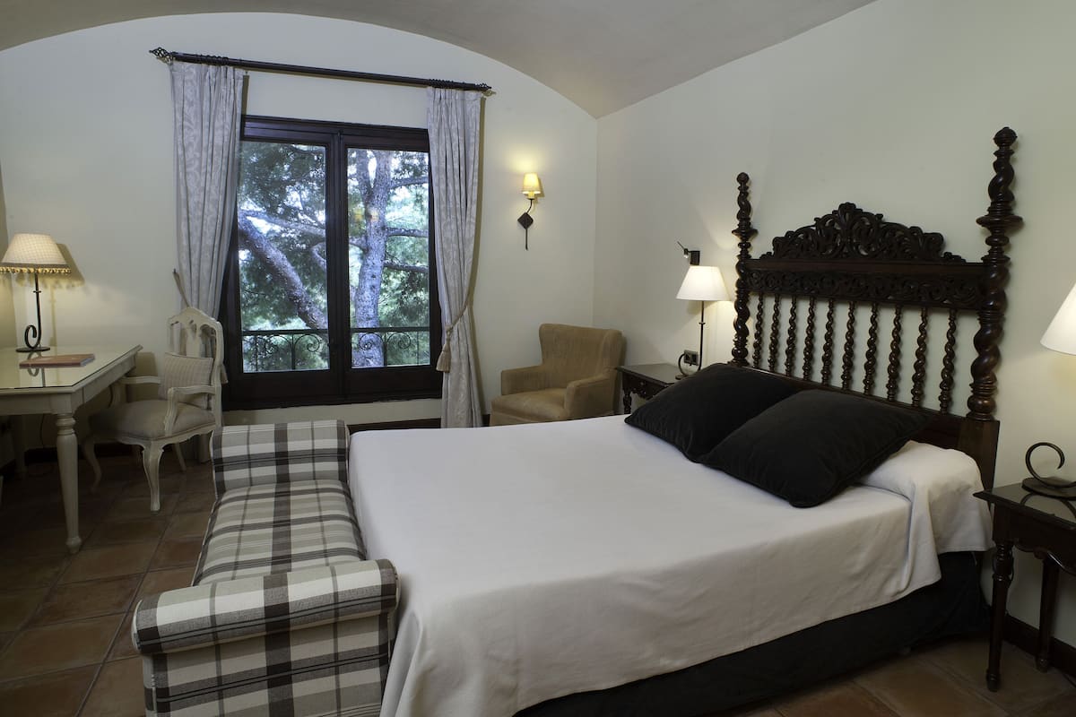 A hotel room with a bed, a desk, a chair, and a window with curtains.