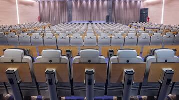 A large auditorium with rows of seats, a stage, and curtains.