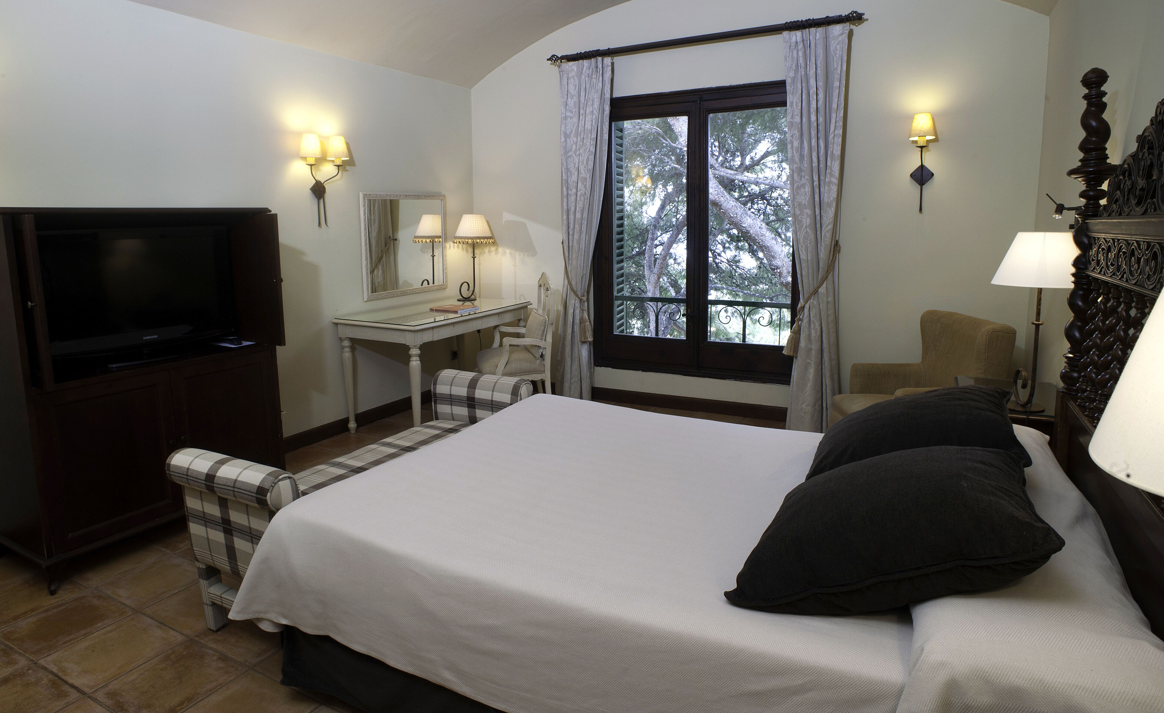 A hotel room with a bed, a desk, a chair, a television, and a window with curtains.