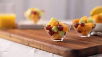 Ein Holzservierbrett mit drei klaren Glasbehältern, gefüllt mit einem Obstsalat.
