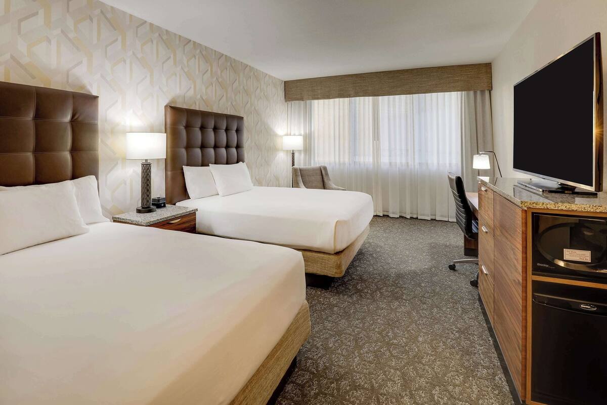 A hotel room with two beds, a TV, a desk, and a minibar.