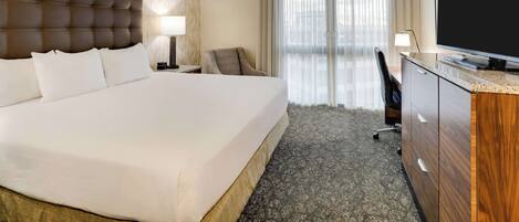 A hotel room with a large bed, a desk, a television, and a view of the outdoors through the window.