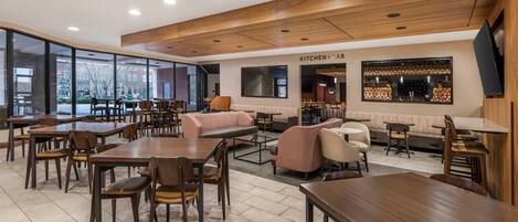 Een modern restaurant met houten tafels en stoelen, een bar in de keuken en grote ramen met uitzicht op de stad.