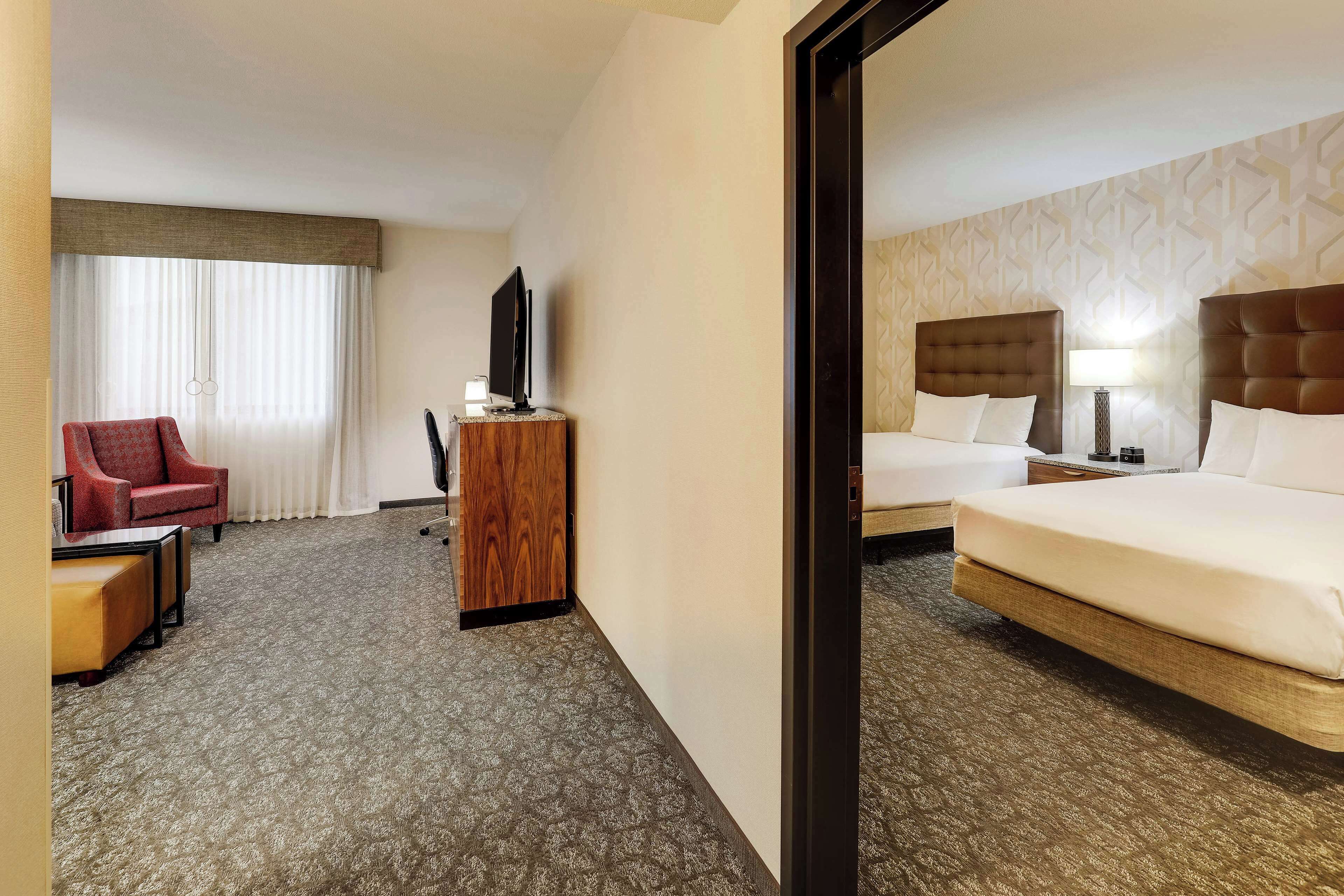 A hotel room with a bed, a TV, a desk, a chair, and a window with curtains.