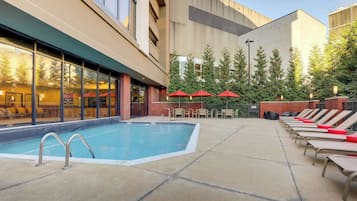 A swimming pool with lounge chairs and umbrellas, surrounded by a building with large windows and a brick facade.