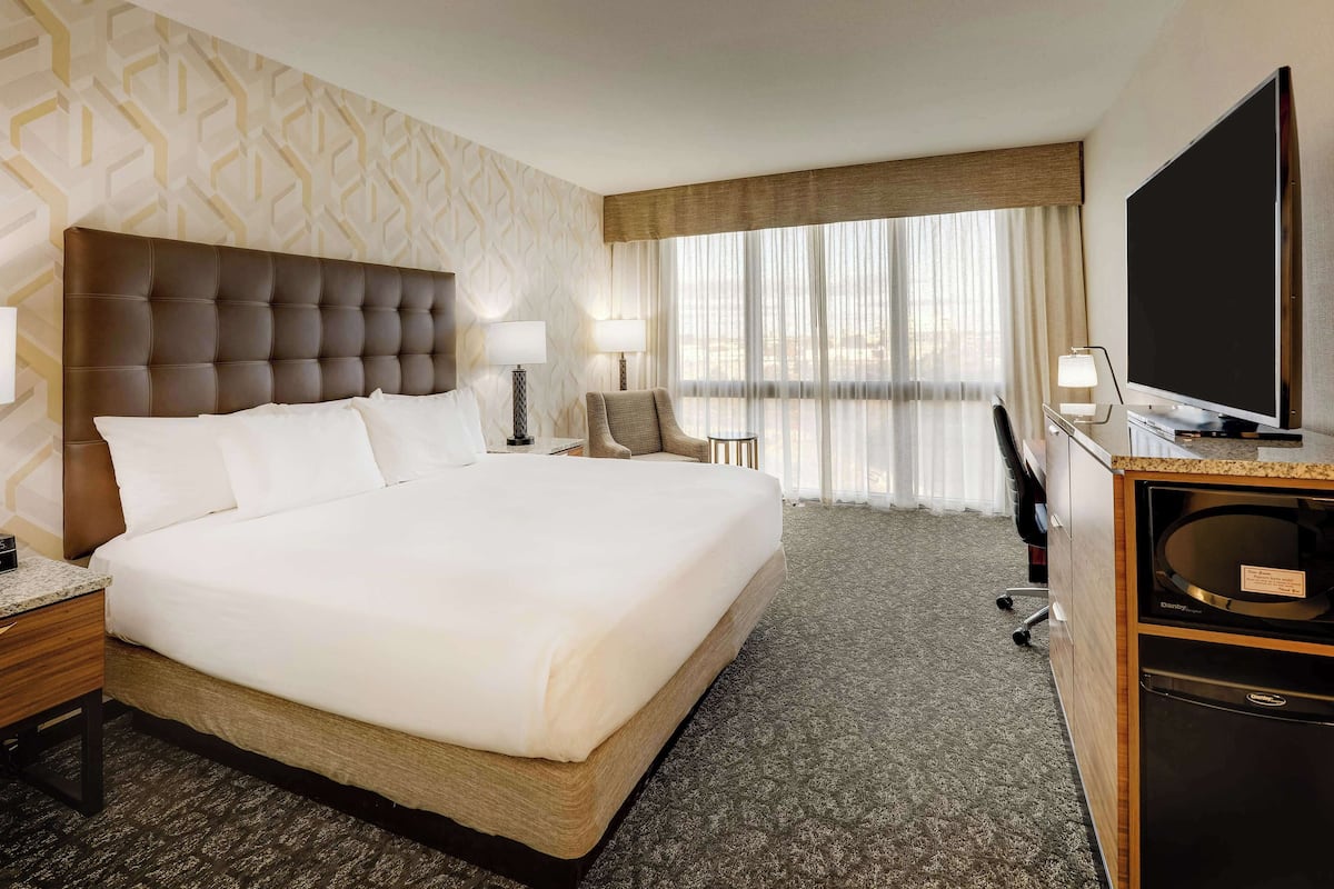 Une chambre d’hôtel dotée d’un grand lit, de deux tables de chevet, d’un bureau avec un téléviseur à écran plat et offrant une vue sur la ville grâce à de grandes fenêtres.
